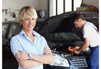 a woman standing in front of a car shop as a man inspects it